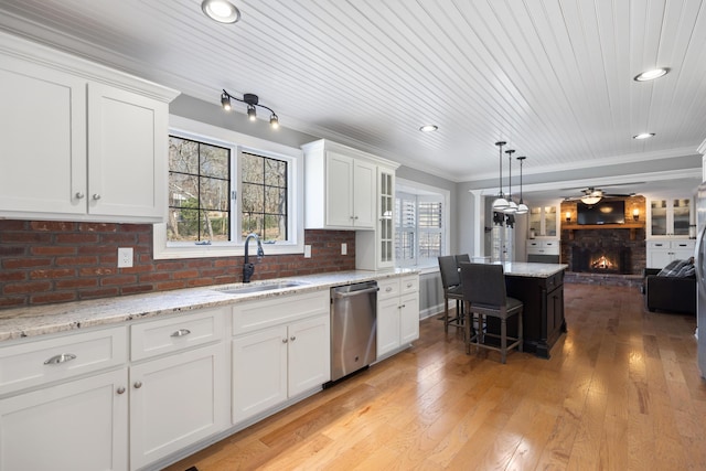 kitchen featuring a sink, a stone fireplace, stainless steel dishwasher, crown molding, and open floor plan