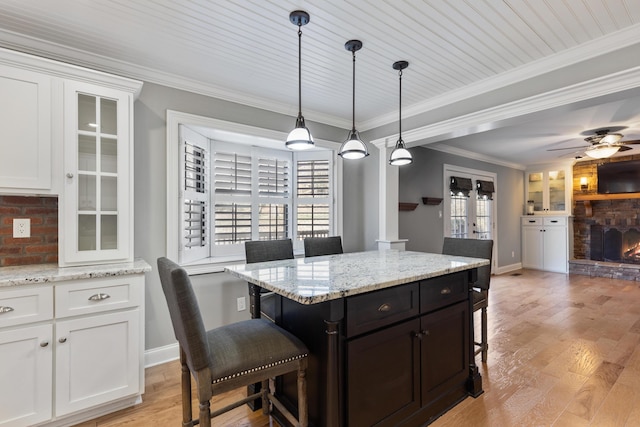 kitchen with a breakfast bar area, light wood-style flooring, a fireplace, white cabinetry, and crown molding