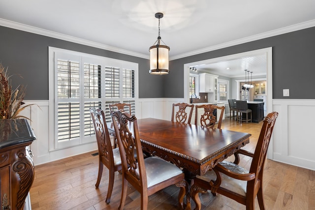 dining space with light wood-type flooring, a wainscoted wall, and a decorative wall