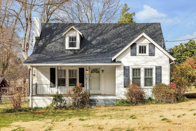 view of front of home with a chimney, a porch, a shingled roof, and a front yard