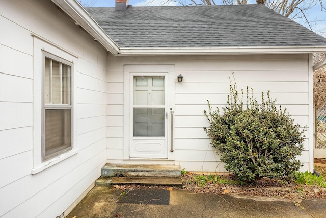 doorway to property featuring a chimney and a shingled roof