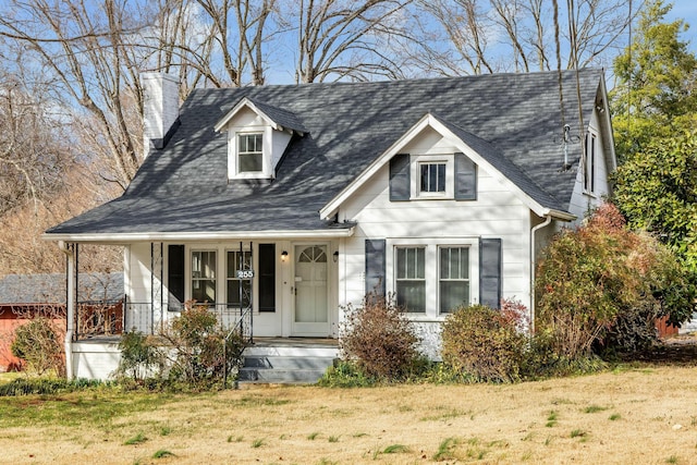 view of front facade with a porch, a chimney, a front yard, and roof with shingles