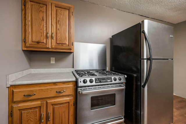 kitchen with wood finished floors, brown cabinetry, light countertops, appliances with stainless steel finishes, and a textured ceiling