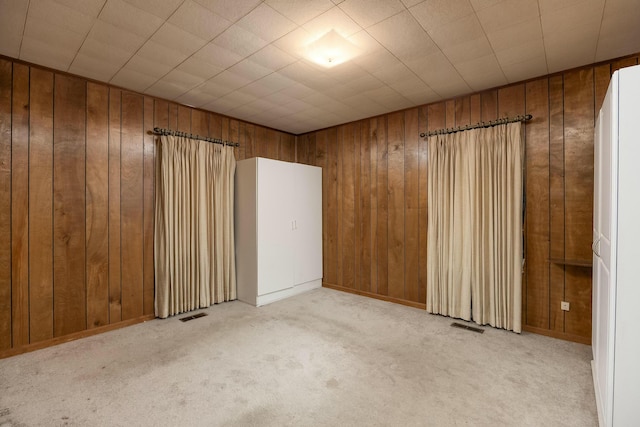 empty room featuring visible vents, wood walls, and carpet floors