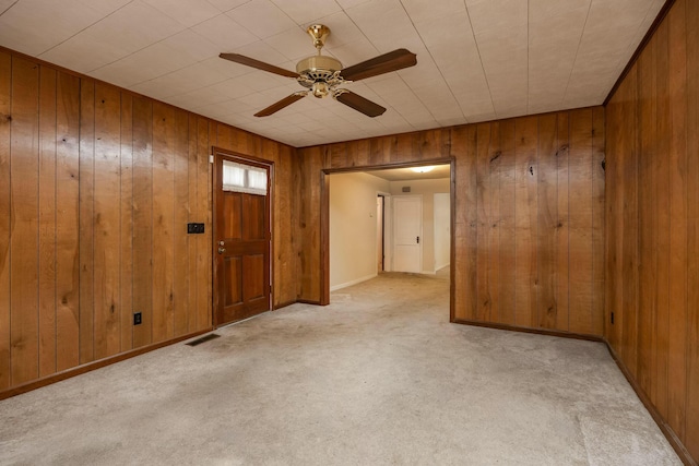 spare room featuring visible vents, baseboards, ceiling fan, wood walls, and carpet floors