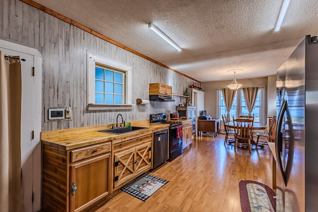 kitchen featuring pendant lighting, wood counters, black appliances, sink, and light hardwood / wood-style floors