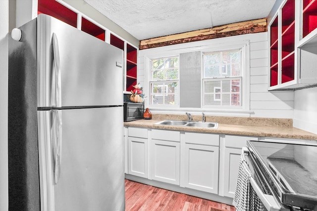 kitchen with stove, sink, light hardwood / wood-style floors, white cabinetry, and stainless steel refrigerator