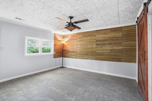 spare room with wooden walls, ceiling fan, a barn door, and dark carpet