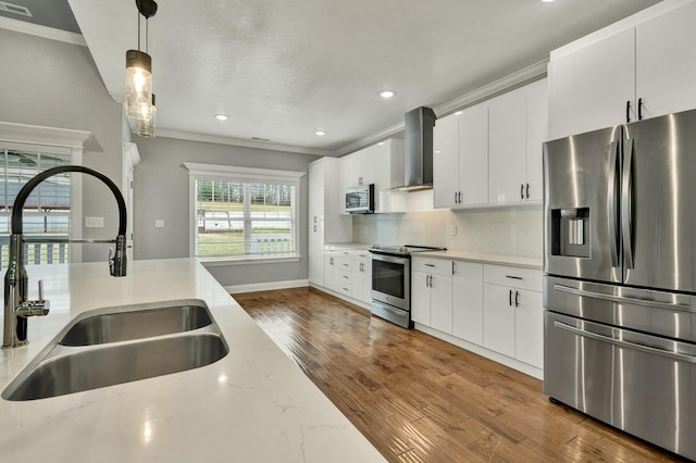 kitchen with appliances with stainless steel finishes, sink, white cabinets, hanging light fixtures, and wall chimney range hood