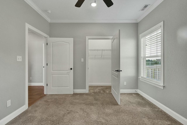 unfurnished bedroom featuring a walk in closet, ceiling fan, crown molding, light carpet, and a closet