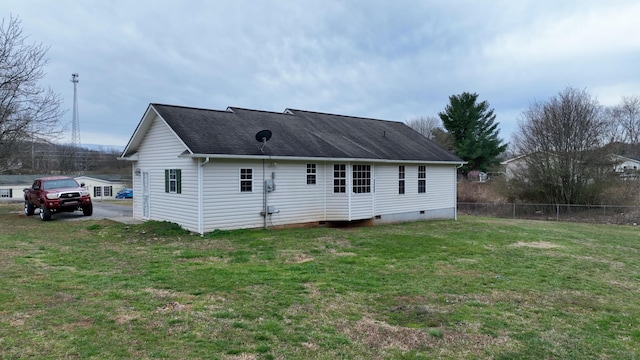 rear view of property featuring crawl space, a lawn, a shingled roof, and fence