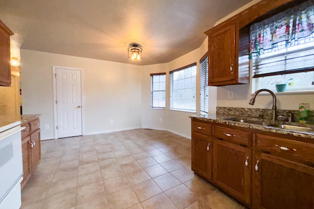 kitchen with brown cabinets, a sink, stone countertops, light tile patterned floors, and baseboards