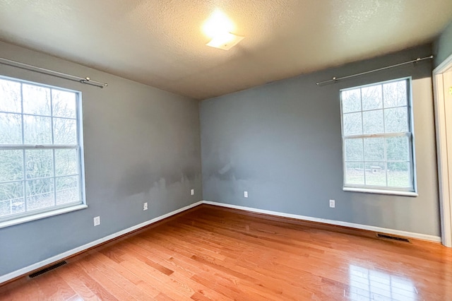 spare room featuring visible vents, baseboards, a textured ceiling, and wood finished floors