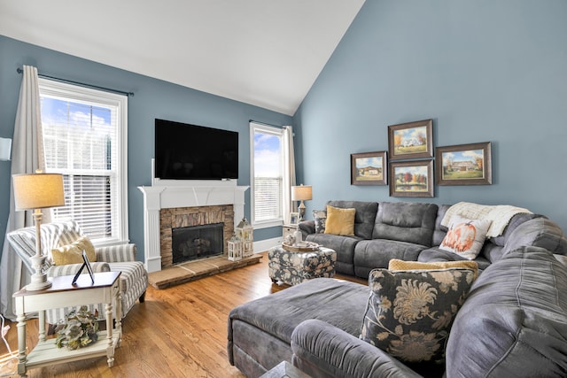 living room featuring hardwood / wood-style floors, vaulted ceiling, a stone fireplace, and a wealth of natural light