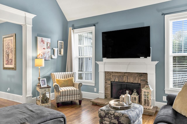 living room featuring wood-type flooring, vaulted ceiling, a stone fireplace, and plenty of natural light