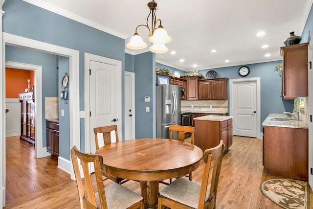 dining space featuring light hardwood / wood-style floors, ornamental molding, sink, and an inviting chandelier