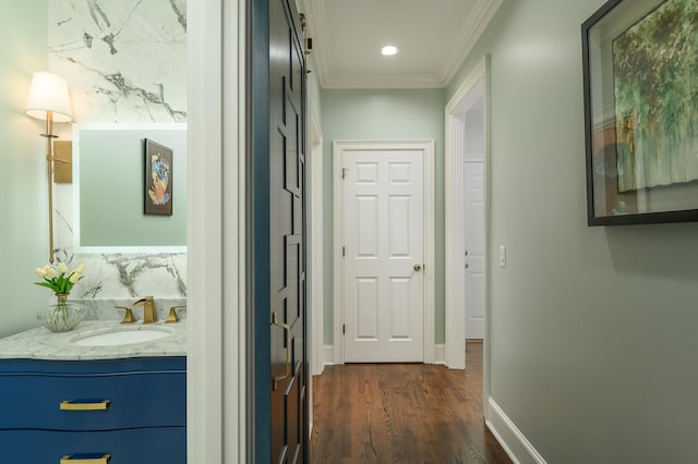 corridor featuring a sink, dark wood finished floors, recessed lighting, baseboards, and ornamental molding