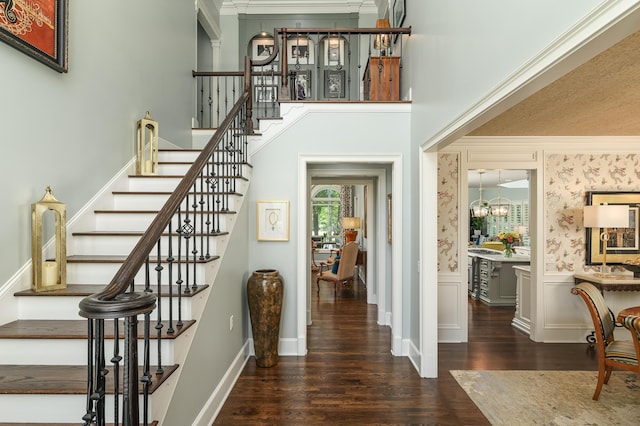 foyer entrance featuring wainscoting, wood finished floors, stairway, an inviting chandelier, and ornamental molding