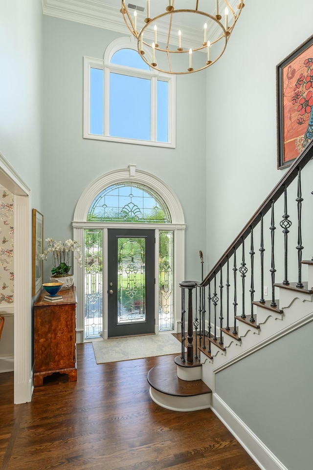 entrance foyer with ornamental molding, wood finished floors, baseboards, a high ceiling, and a chandelier