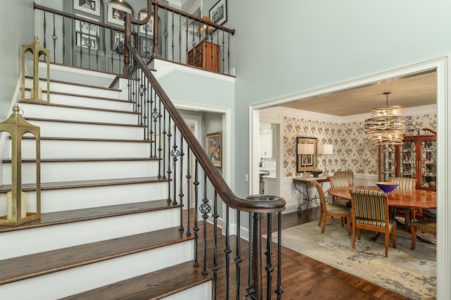 stairway featuring crown molding, wood finished floors, a wainscoted wall, an inviting chandelier, and wallpapered walls