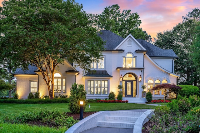 french country style house with brick siding, a shingled roof, and a front yard