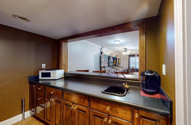 kitchen with baseboards, brown cabinetry, dark countertops, white microwave, and a sink