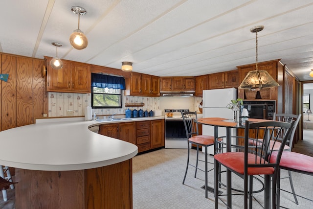kitchen featuring brown cabinets, a sink, light countertops, a peninsula, and white appliances