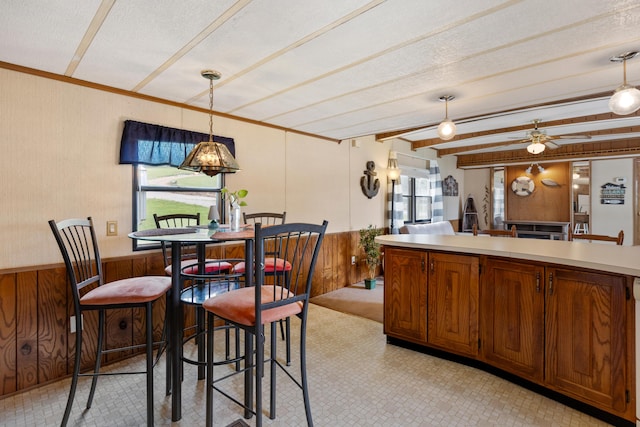 dining area with crown molding, a wainscoted wall, wood walls, and beam ceiling