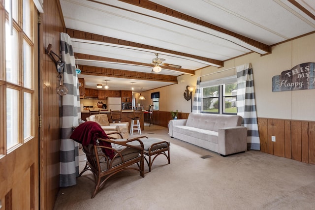 living area with wooden walls, light colored carpet, and beam ceiling