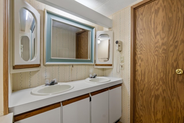 full bathroom with double vanity, a sink, and wallpapered walls