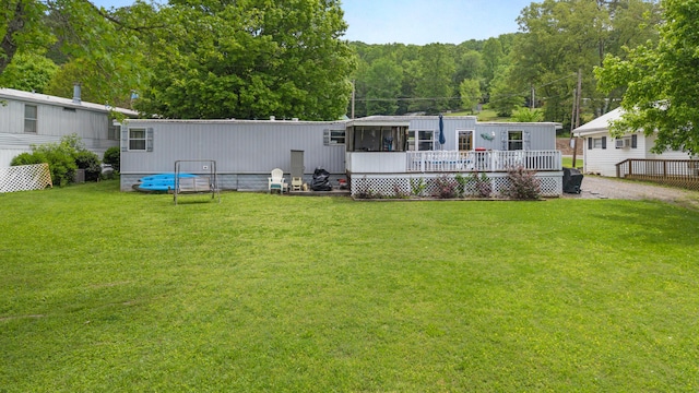 rear view of house with a lawn, a deck, and a forest view