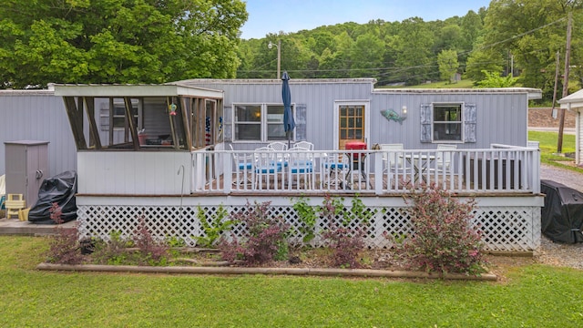 back of property featuring a yard, a view of trees, and a wooden deck