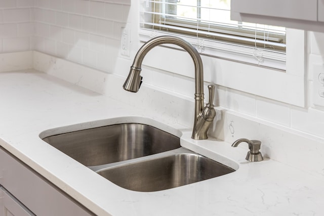 interior details featuring sink, decorative backsplash, and light stone countertops