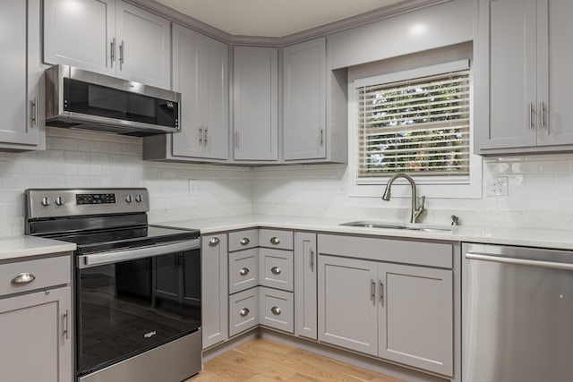 kitchen with sink, gray cabinetry, light hardwood / wood-style flooring, appliances with stainless steel finishes, and backsplash