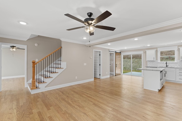 unfurnished living room featuring light hardwood / wood-style floors, ceiling fan, a barn door, and ornamental molding