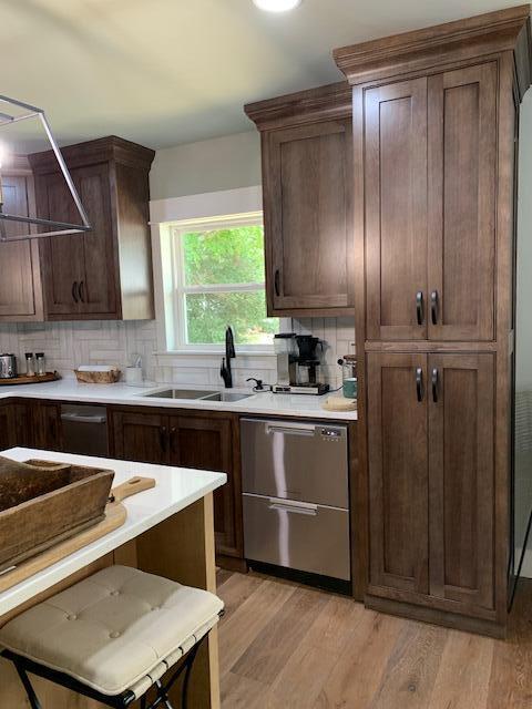 kitchen with backsplash, sink, light hardwood / wood-style flooring, stainless steel dishwasher, and dark brown cabinetry