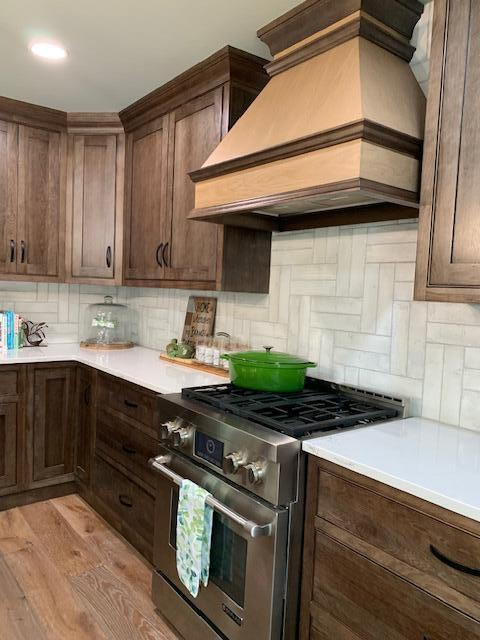 kitchen with backsplash, premium range hood, dark brown cabinets, light hardwood / wood-style flooring, and high end stainless steel range