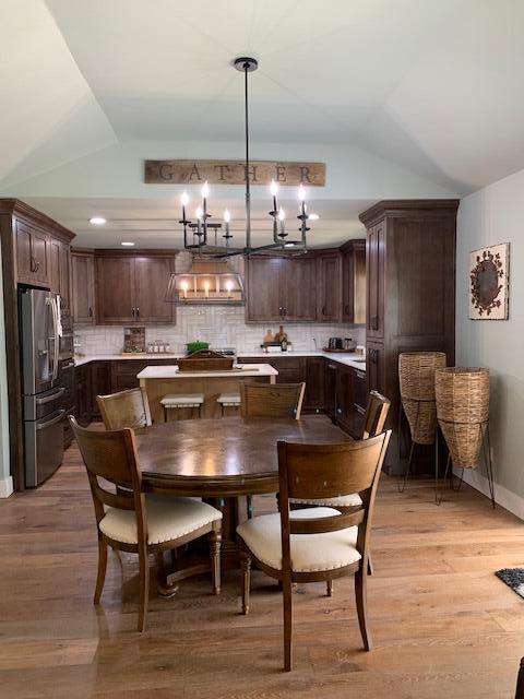 dining room featuring a notable chandelier, vaulted ceiling, and light wood-type flooring