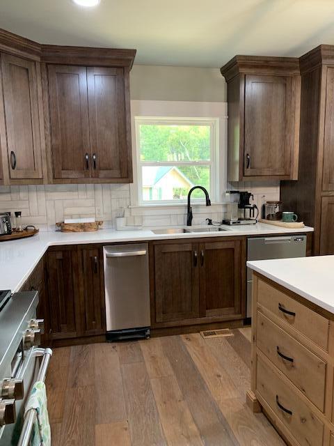 kitchen with dark brown cabinetry, sink, stainless steel appliances, tasteful backsplash, and light hardwood / wood-style floors