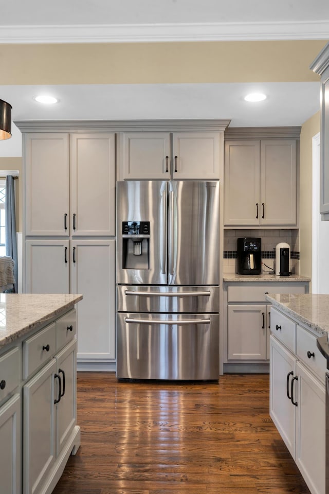 kitchen with light stone counters, dark wood-style floors, crown molding, stainless steel fridge, and backsplash