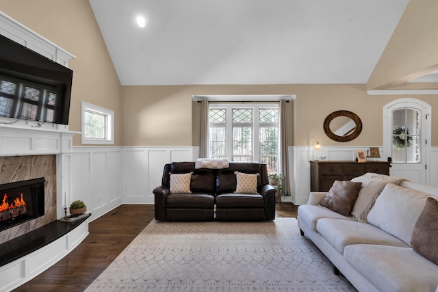 living room with a wainscoted wall, lofted ceiling, dark wood-type flooring, and a high end fireplace