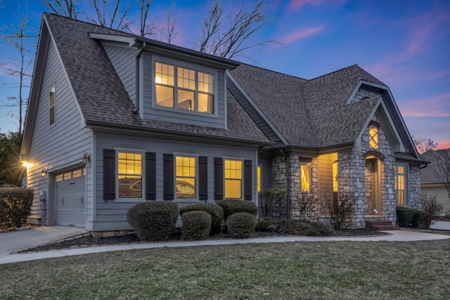 view of front facade with stone siding, a lawn, driveway, and roof with shingles