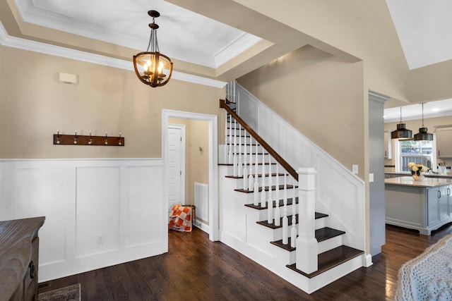 staircase featuring visible vents, crown molding, wood finished floors, a notable chandelier, and a raised ceiling