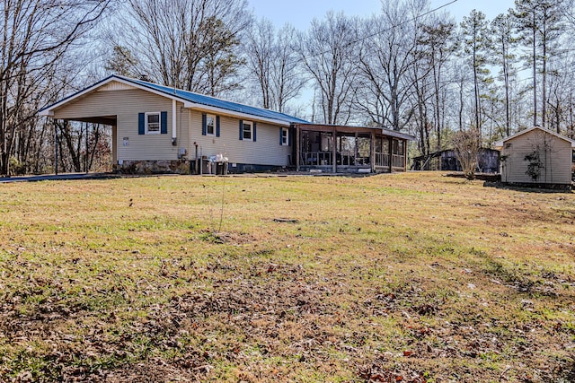 back of house featuring a storage unit, a carport, a yard, and a sunroom