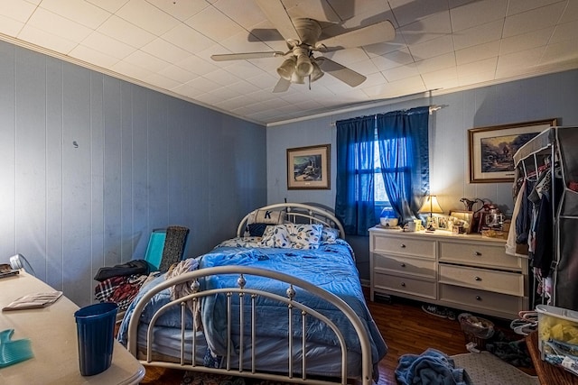 bedroom with ceiling fan, dark hardwood / wood-style flooring, ornamental molding, and wooden walls