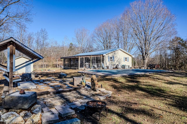 rear view of house with a covered pool, an outdoor fire pit, a sunroom, and a patio