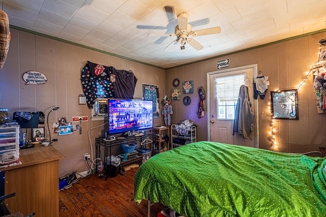 bedroom with ceiling fan, wood walls, and wood-type flooring