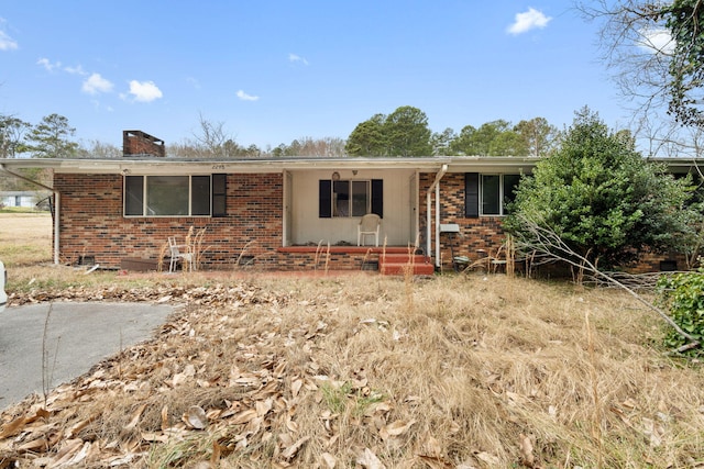 ranch-style home with brick siding, a chimney, and a porch