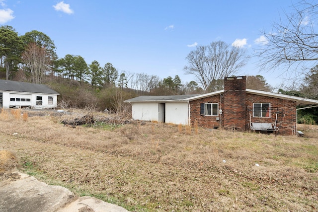 view of property exterior featuring a chimney, an outdoor structure, and brick siding