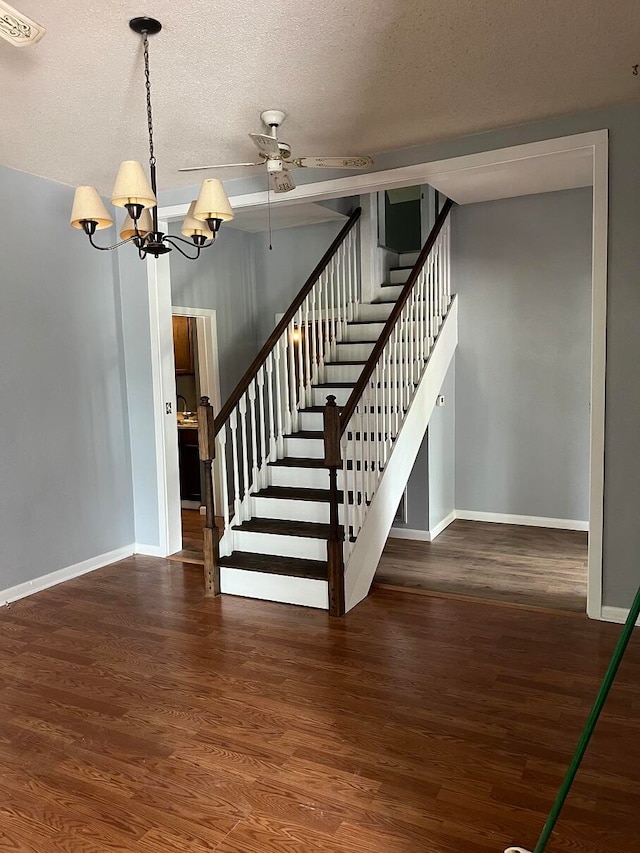 stairs featuring ceiling fan with notable chandelier, wood-type flooring, and a textured ceiling